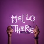 Bright neon sign saying 'Hello There' held by hands against a purple background.